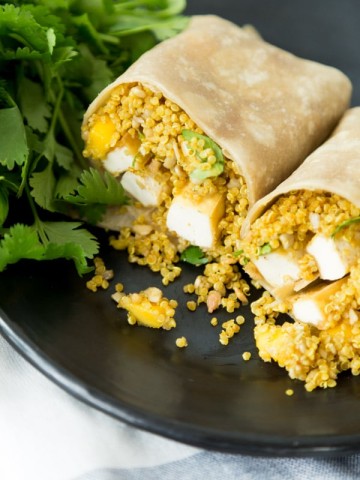 A wrap with tofu and quinoa on a black plate