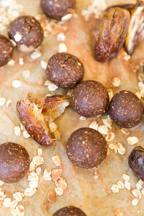 Chocolate energy bites on parchment paper with dates and whole oats scattered around