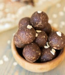 A clear mason jar filed with chocolate energy balls and rolled oats sprinkles around a wood table