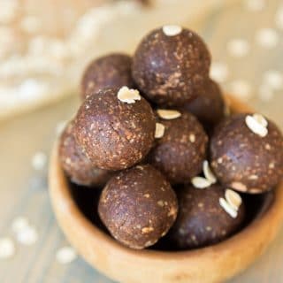 A clear mason jar filed with chocolate energy balls and rolled oats sprinkles around a wood table