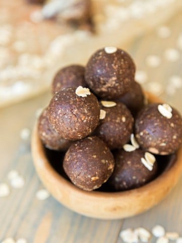 A clear mason jar filed with chocolate energy balls and rolled oats sprinkles around a wood table