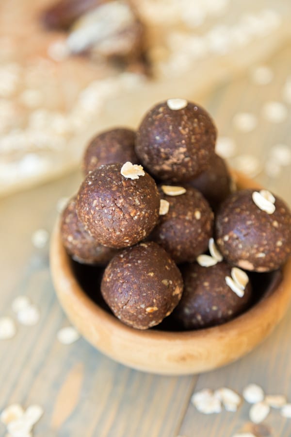 A clear mason jar filed with chocolate energy balls and rolled oats sprinkles around a wood table