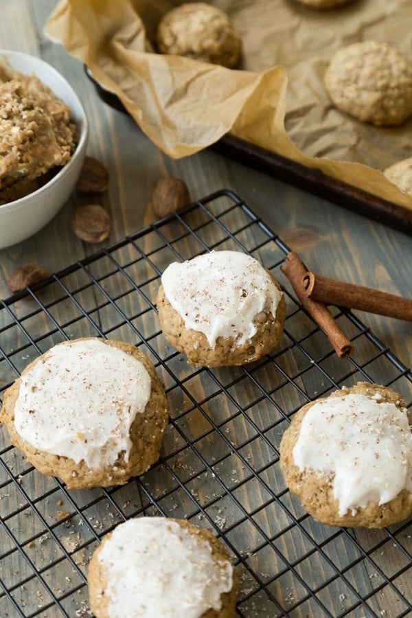 apple oat cookies on a cooling rack frosted with cinnamon sticks and dough in the background