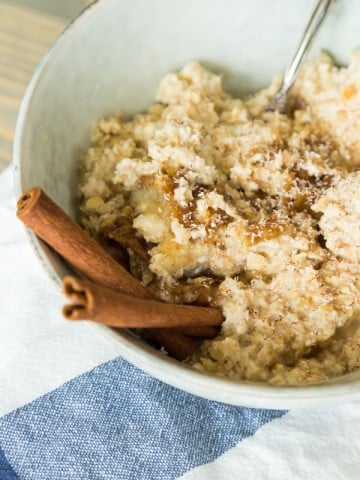 apple cinnamon overnight oats with cinnamon sticks, blue bowl, and napkin on wood board