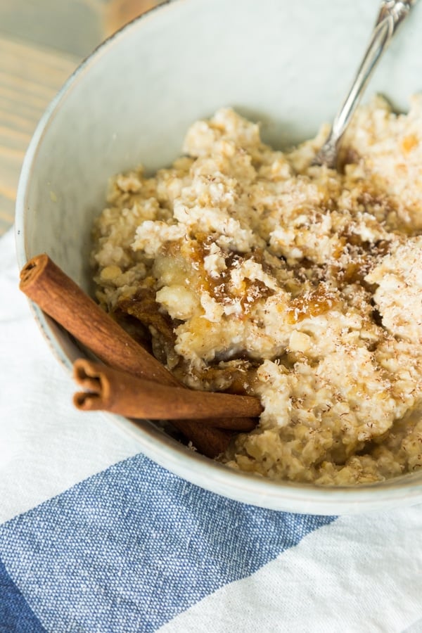 apple cinnamon overnight oats with cinnamon sticks, blue bowl, and napkin on wood board