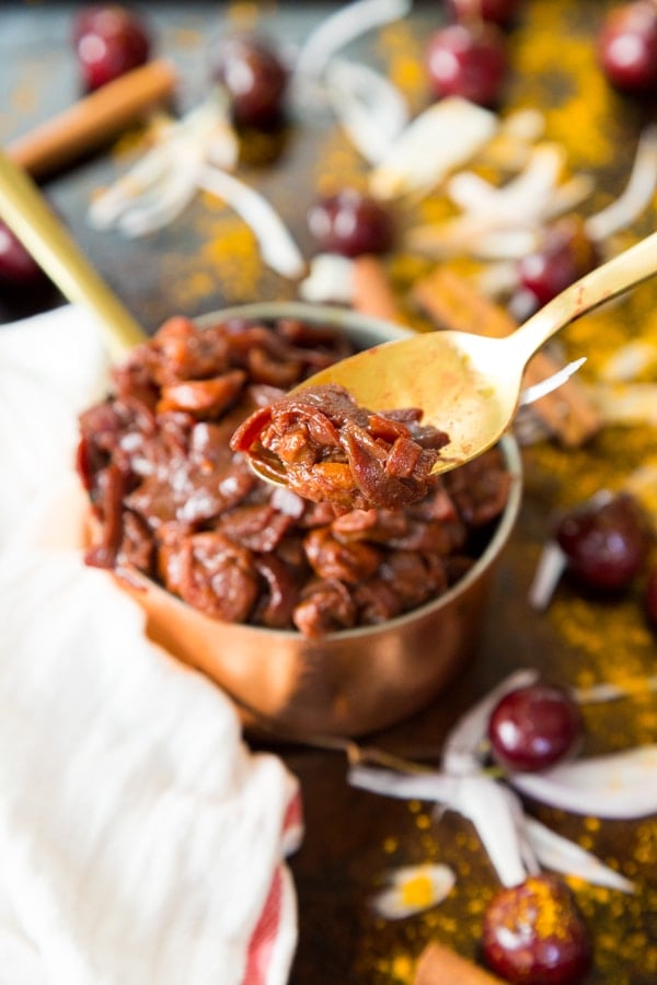 Cherry Onion confit on a gold spoon in front of a copper pot