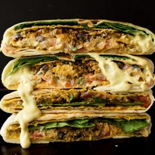 Four halves of vegan crunchwrap supremes stacked on to of each other with vegan cheese sauce dripping down the sides.