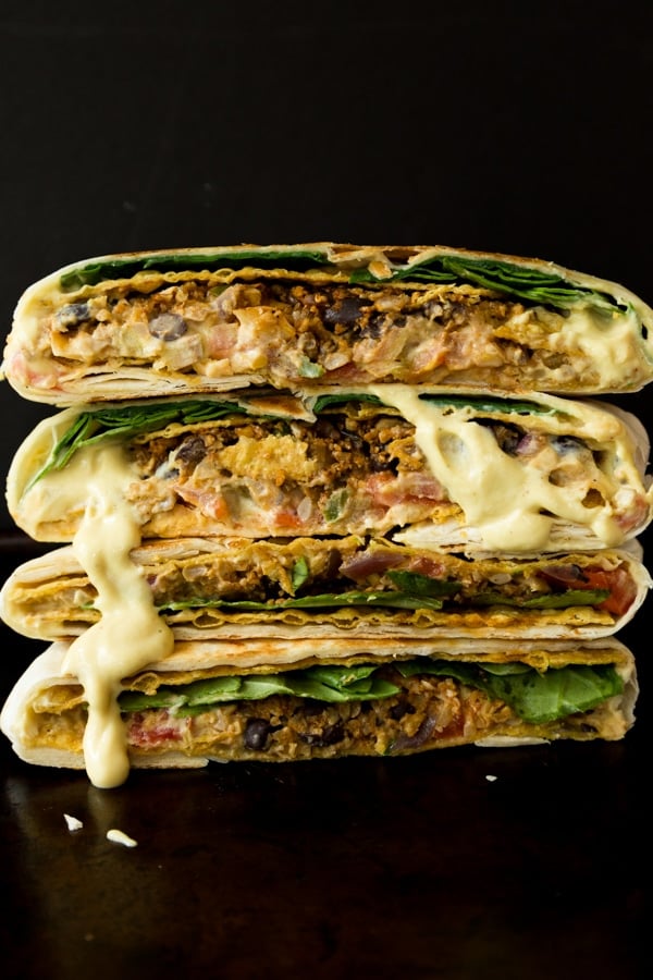 Four halves of vegan crunchwrap supremes stacked on to of each other with vegan cheese sauce dripping down the sides.