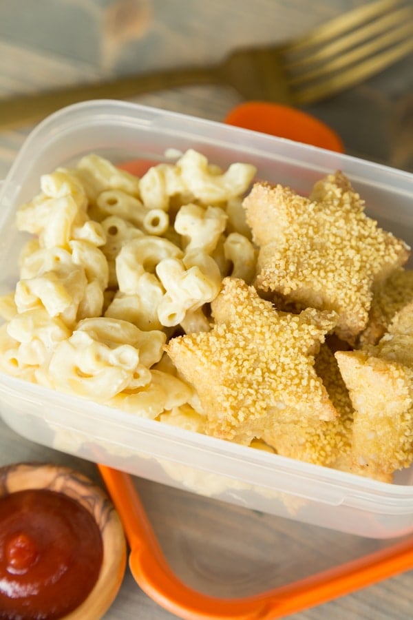 Vegan tofu chik'n nuggets in a star shape with mac 'n' cheese in a portable box with a small wood bowl of ketchup next to it