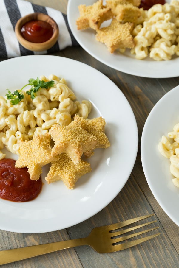 Vegan star shaped chik'n nuggets and mac 'n'cheese on white plates with ketchup