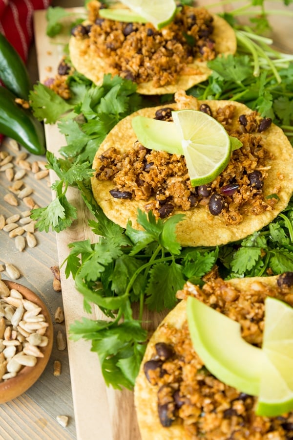 Healthy vegan taco filling on three corn tostados with vegan cheese sauce and chopped greens on a wood board