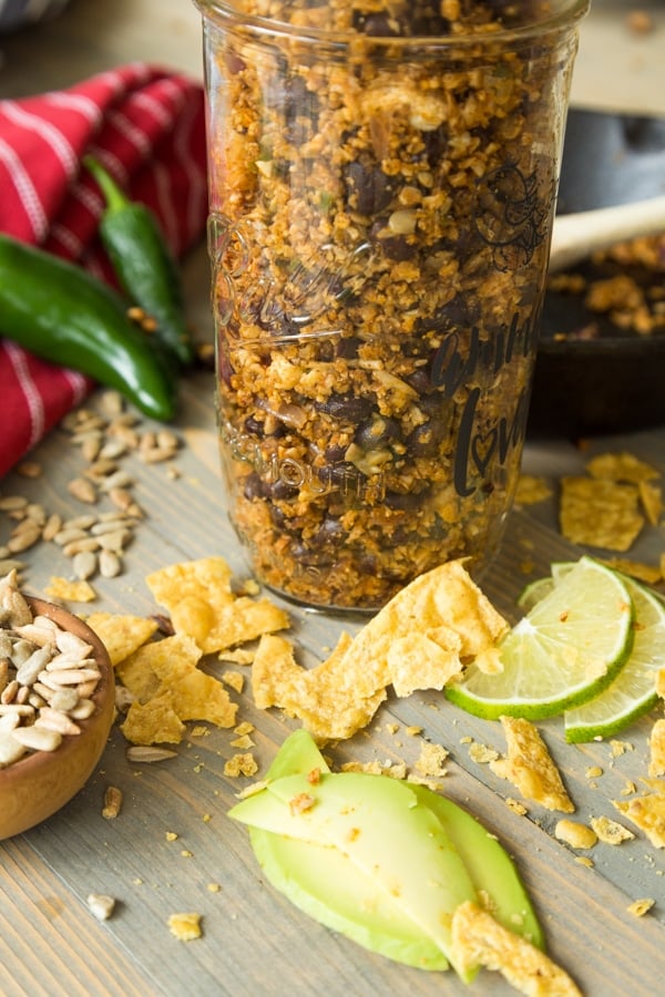 Vegan taco filling in a mason jar with crumbled corn chips, sliced limes, and sunflower seeds and vegetables next to the jar