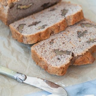 A loaf of banana bread sliced on parchment paper with pads of butter and a butter knife next to the bread