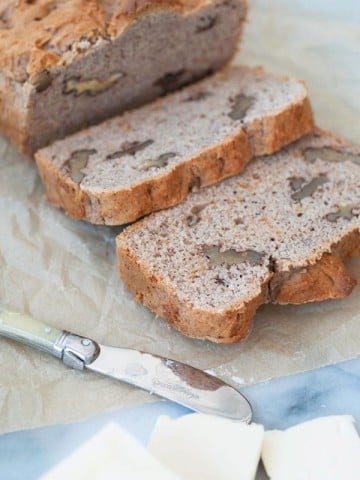 A loaf of banana bread sliced on parchment paper with pads of butter and a butter knife next to the bread