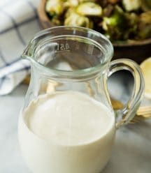 Caesar Dressing in a glass container with the brussels sprout salad behind it