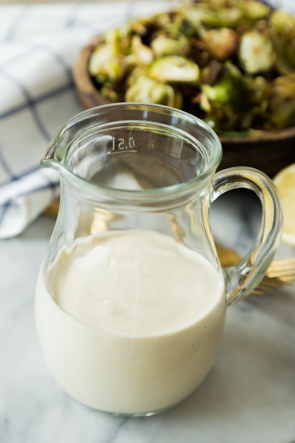 Caesar Dressing in a glass container with the brussels sprout salad behind it