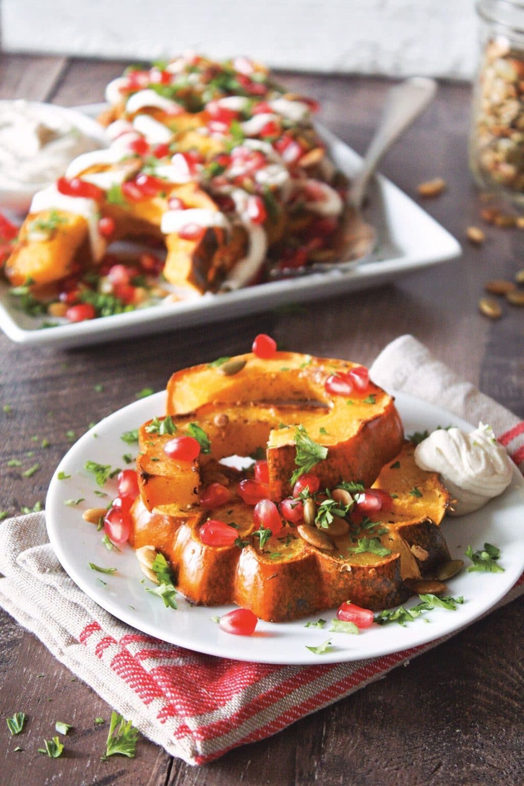 Roasted butternut squash with garam masala on a white plate with a platter of the recipe in the background