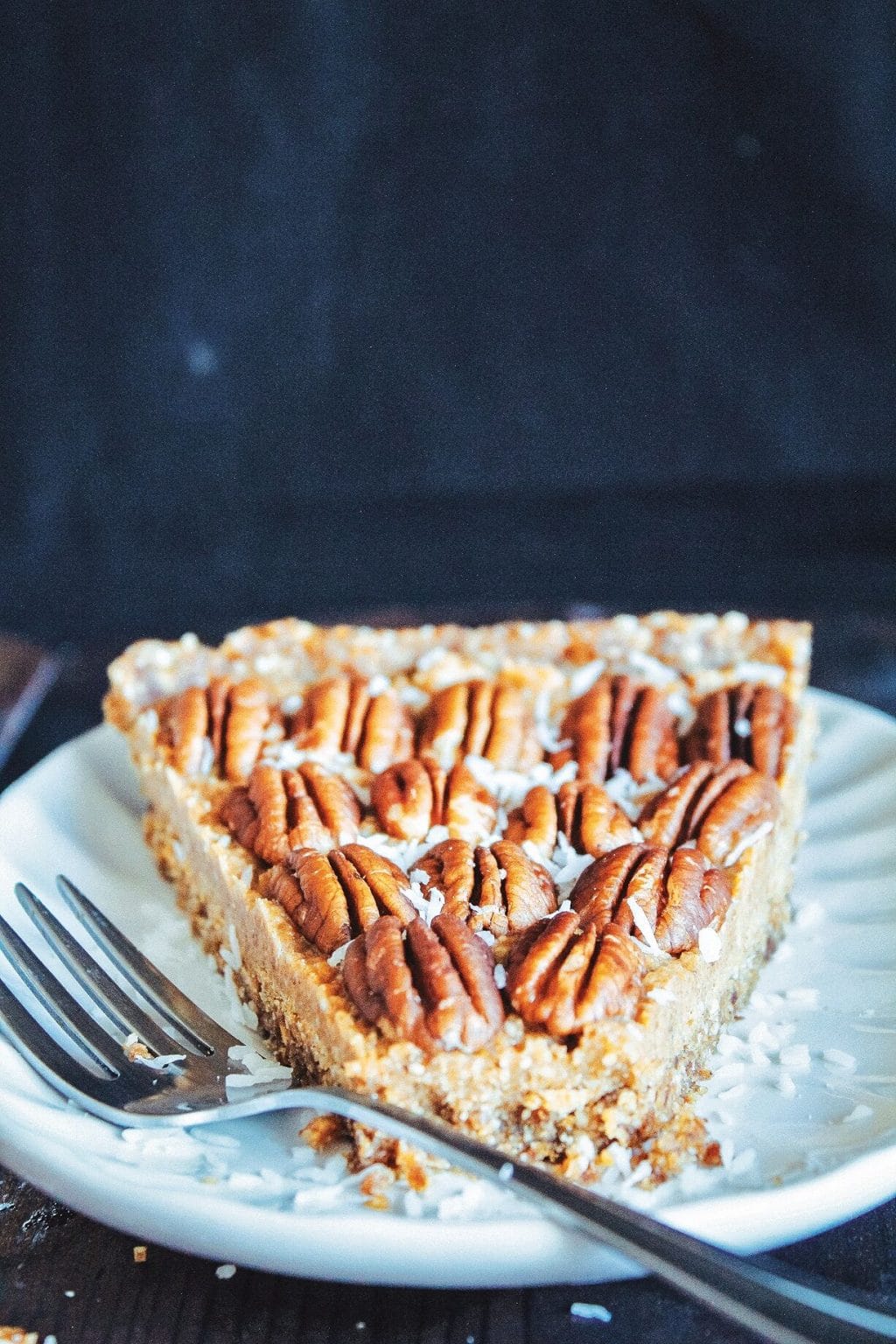 A slice of maple pecan pie on a white plate with a silver fork resting on the edge of the plate