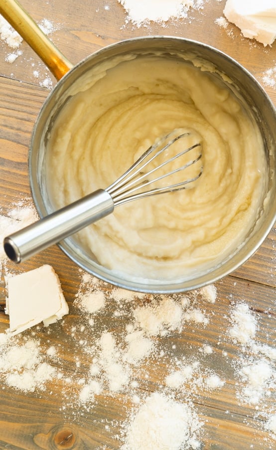 A vegan roux being whisked in a copper pan with flour and butter on the side of the pan