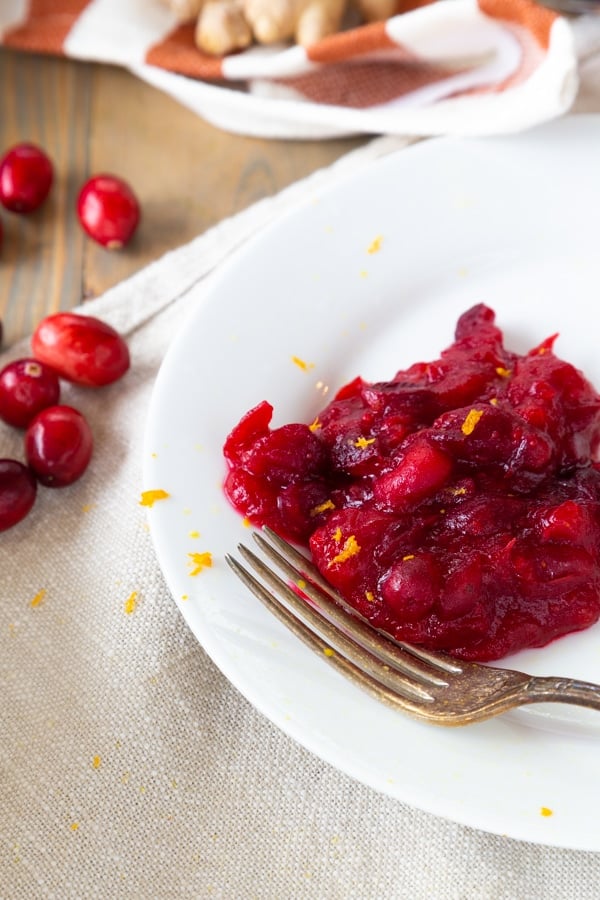 Homemade cranberry sauce on a white plate with a fork resting on the edge and whole cranberries on the side of the plate