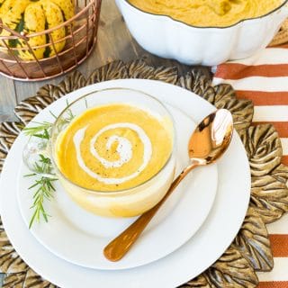 Hannah sweet potato and pumpkin bisque in a clear mug with cashew cream rosemary and a copper basket with an acorn squash