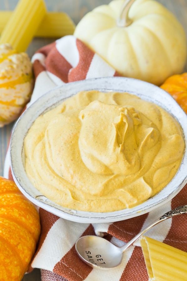 Pumpkin Cashew Filling for stuffed manicotti in a white bowl on a orange and white striped towel with pumpkins surrounding it