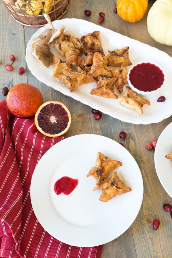Ricotta and shiitake stuffed wontons with cranberry orange dipping sauce on a wooden board with white plates and a red napkin