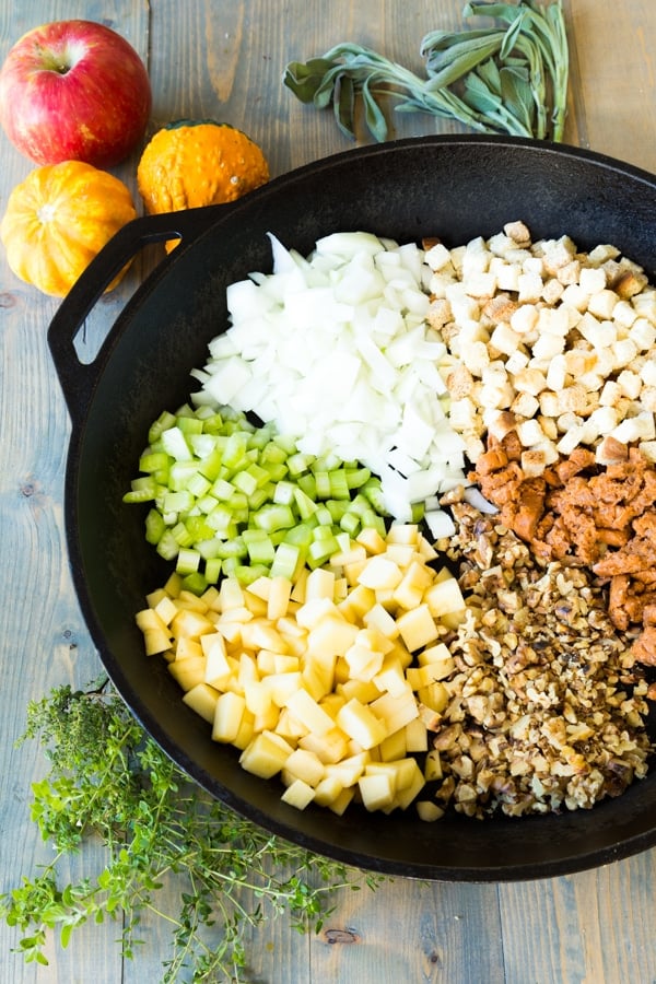 Onions, celery, breadcrumbs, herbs, apples, and breadcrumbs for stuffing in an iron skillet with ingredients on the side of the pan
