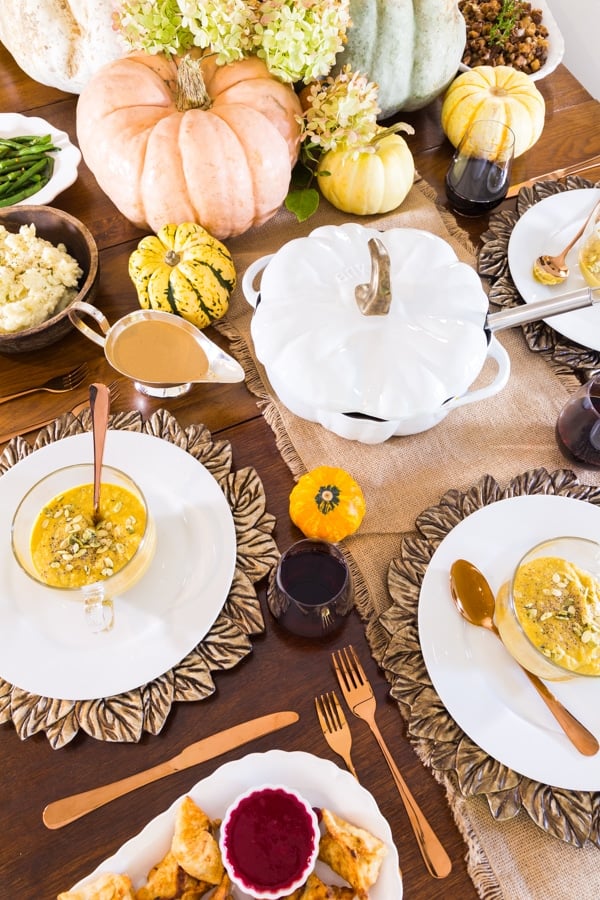 Thanksgiving table setting with white place, leaf chargers, copper flatware, and pumpkins