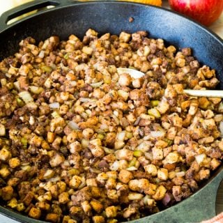 Vegan stuffing in an iron skileet with a spoon in it and a striped towel and apples next to the pan