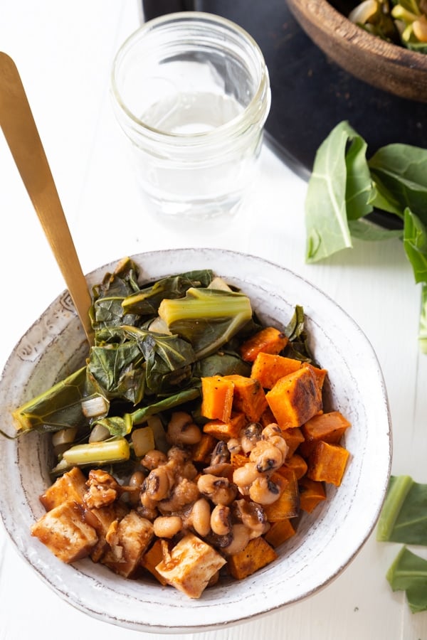 A bowl of BBQ vegetables in a white bowl with a gold fork sticking out of the bowl