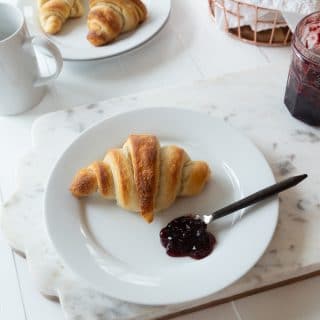 Croissants on white plates on a marble background with a white wood base with blueberry jam