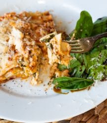A slice of vegan spinach lasagna on a white plate with a side salad.