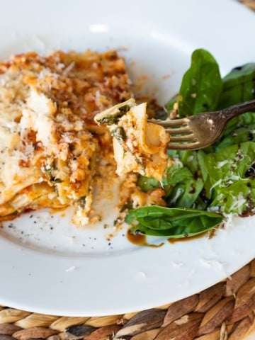 A slice of vegan spinach lasagna on a white plate with a side salad.