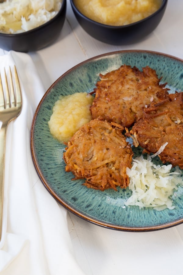 Potato pancakes with apple sauce and sauerkraut on a blue plate with a gold fork