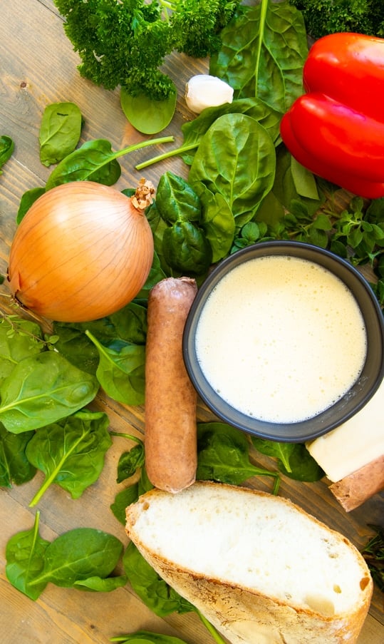 spinach leaves, herbs, onion, a bowl of vegan egg, red bell pepper and bread on a wood table