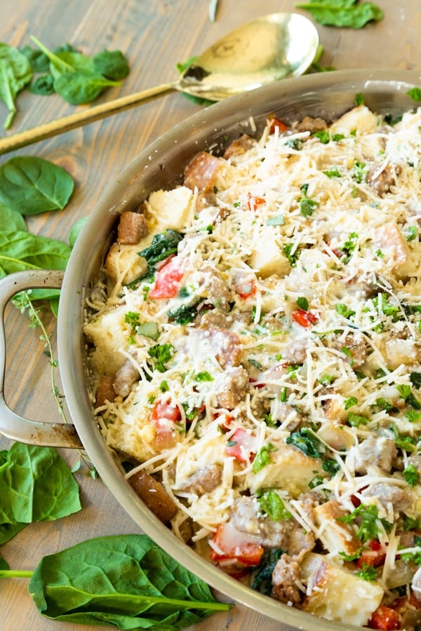 Unbaked vegan strata in a copper round pan with herbs and garlic scattered around it.