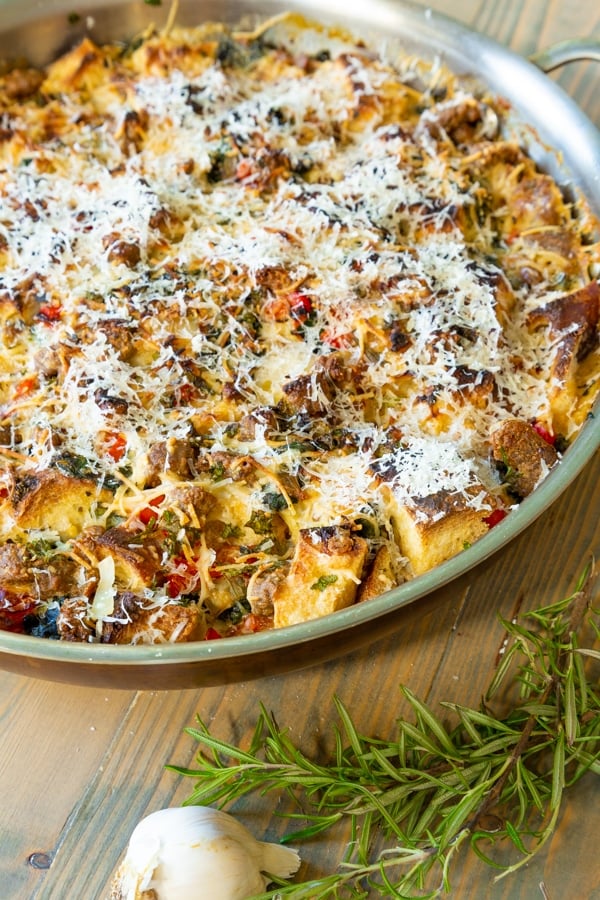 A vegan breakfast casserole in a round copper pan with herbs and garlic next to it