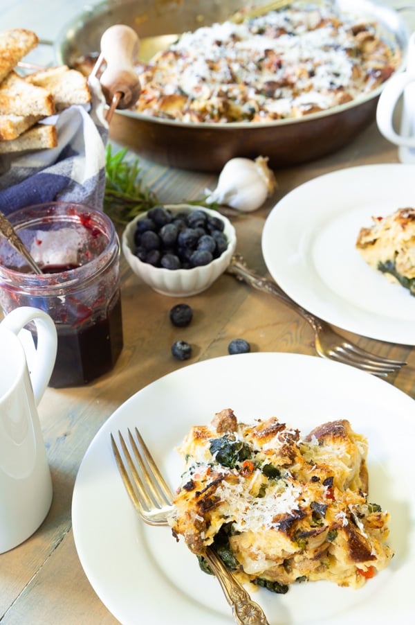 Vegan Strata on white plates with the pan of strata in the background and a jar of preserves and berries on the table