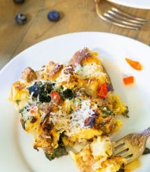 Vegan Strata on a white plate with a gold fork on the edge of the plate and blueberries scattered on a wood table next to the plate