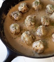 Vegan Swedish meatballs in gravy in a black cast-iron skillet on a white board.