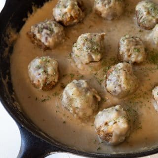 Vegan Swedish meatballs in gravy in a black cast-iron skillet on a white board.