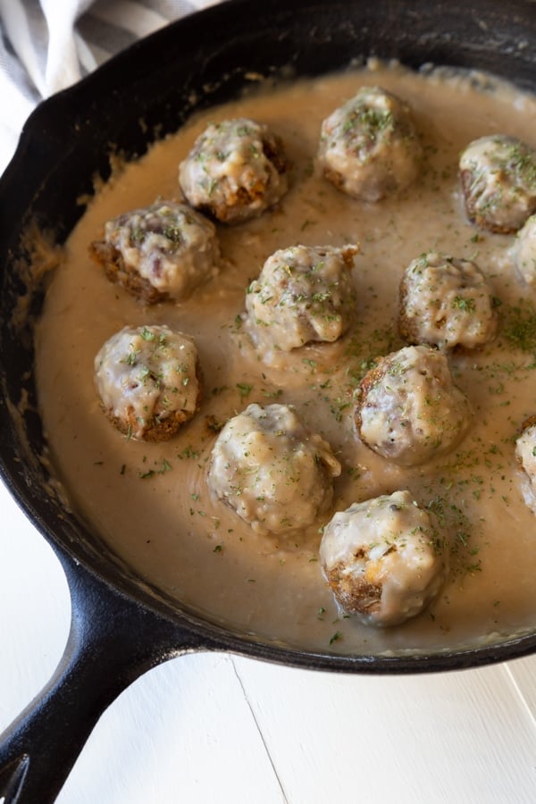 Vegan Swedish meatballs in gravy in a black cast-iron skillet on a white board.