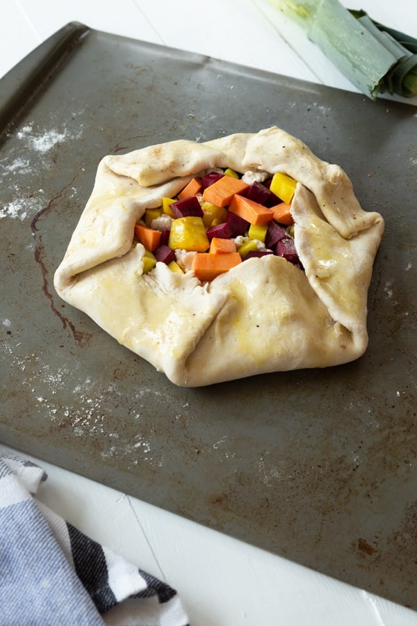 An unbaked sweet potato and beet crostata on a baking sheet with a towel next to it