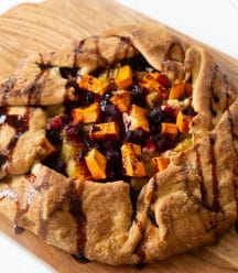 A roasted sweet potato and beet galette drizzled with a balsamic glaze on a wood cutting board