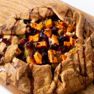 A roasted sweet potato and beet galette drizzled with a balsamic glaze on a wood cutting board