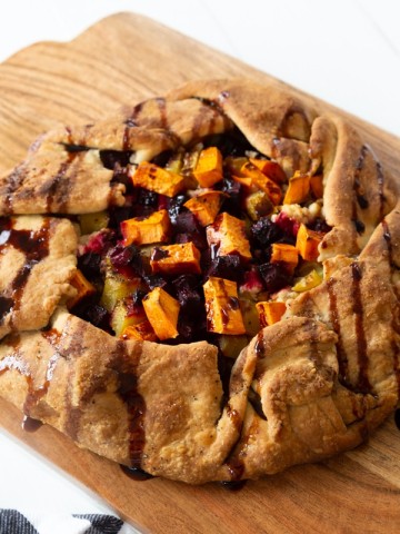 A roasted sweet potato and beet galette drizzled with a balsamic glaze on a wood cutting board