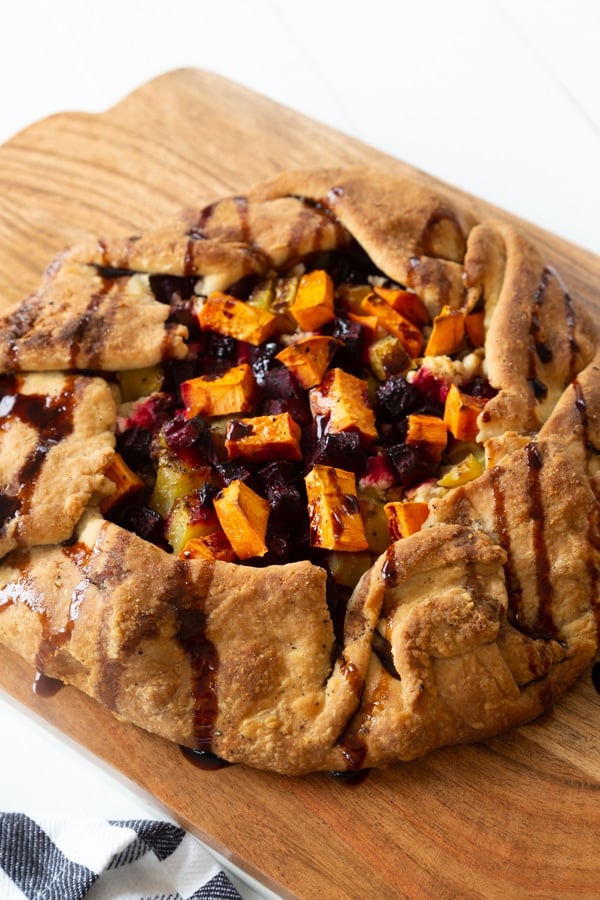 A roasted sweet potato and beet galette drizzled with a balsamic glaze on a wood cutting board