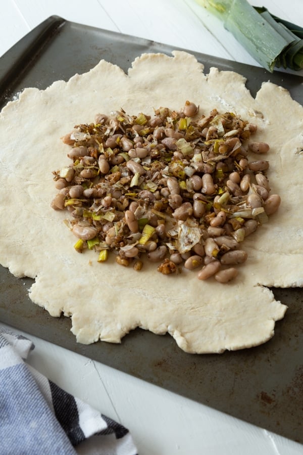 Pie crust rolled out into a circle with a bean and leek filling on top on a baking sheet