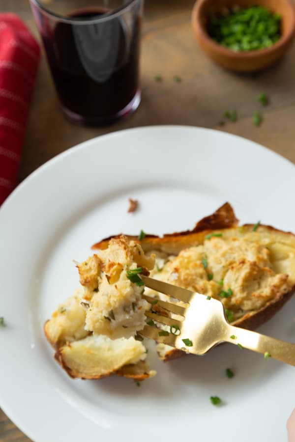 Twice baked ranch potatoes on a wood board with chives, red napkin, gold fork, and a glass of wine